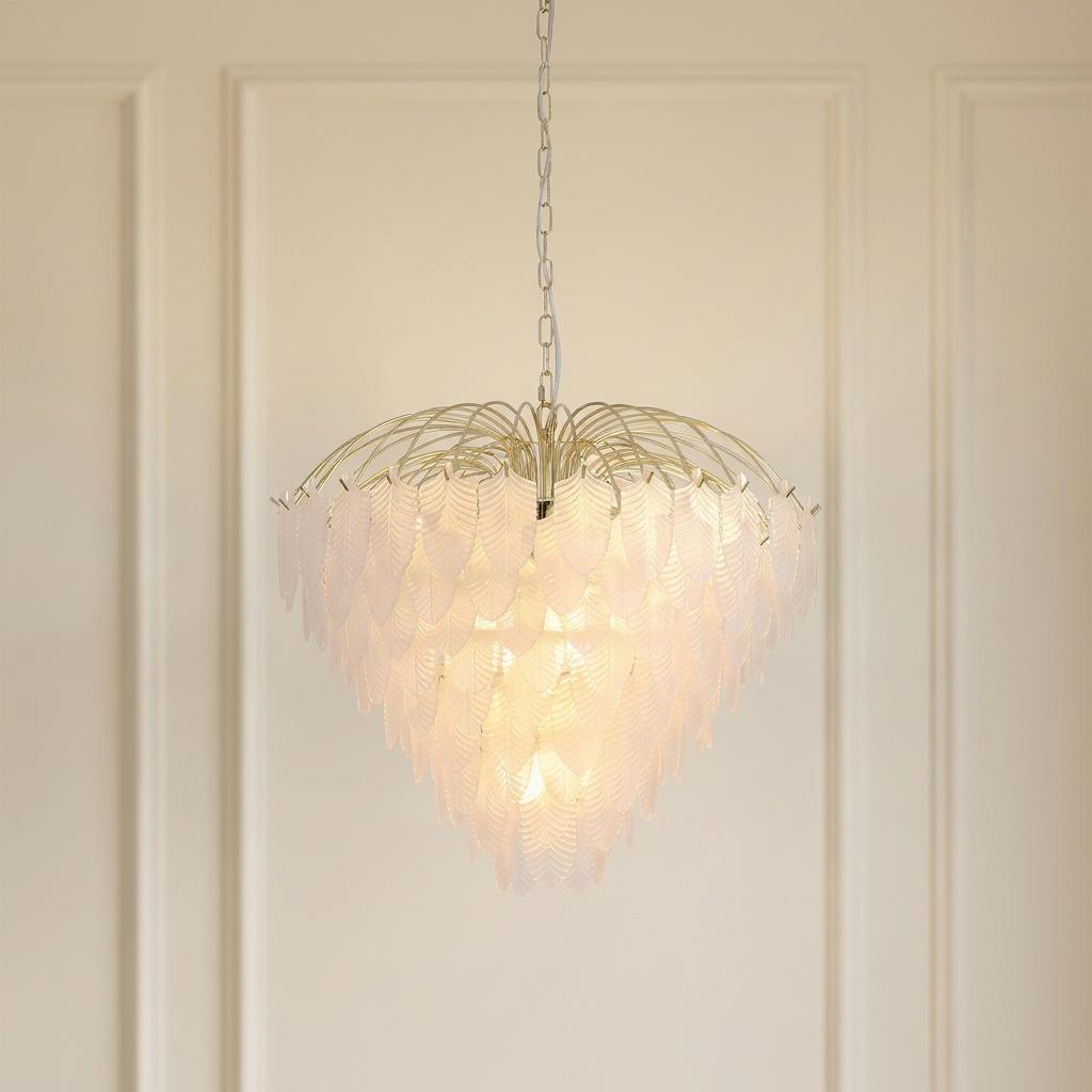 A Feather 10 light polished brass chandelier with frosted glass layers glowing against a cream paneled wall.