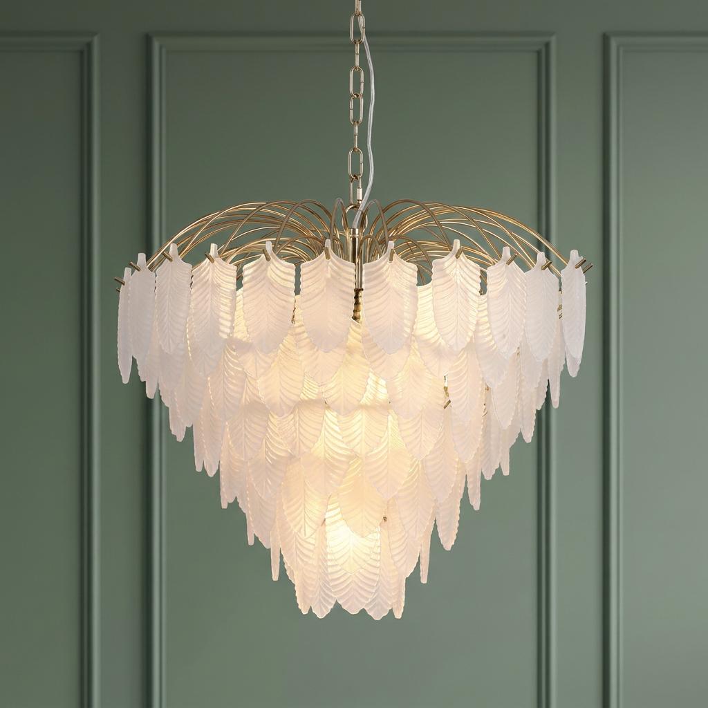 Tiered chandelier with frosted glass feathers on a polished brass frame against a green paneled wall.