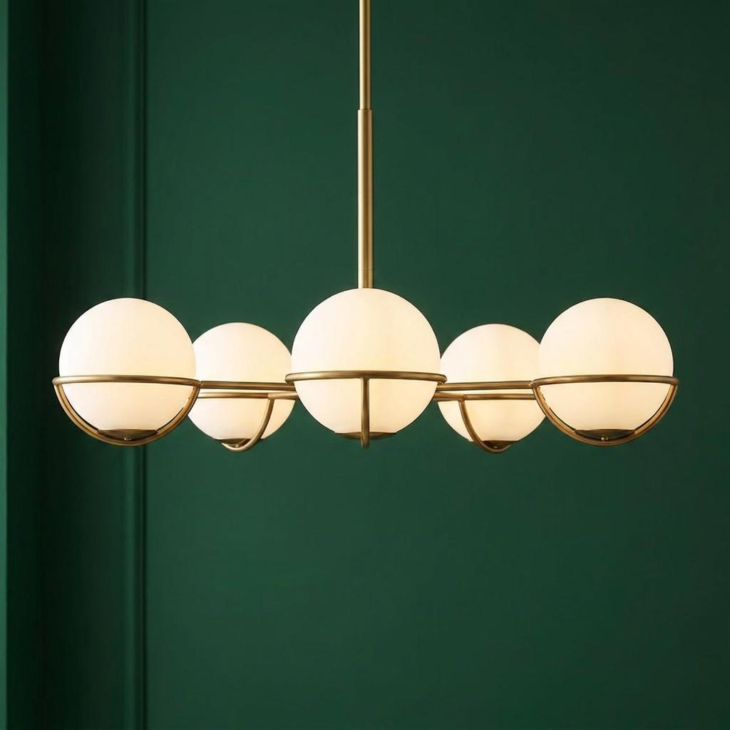 Five white globe light fixtures in burnished brass rings on a chandelier against a dark green wall.