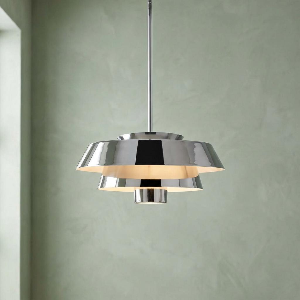 Tiered polished nickel pendant light glowing against a textured light green wall.
