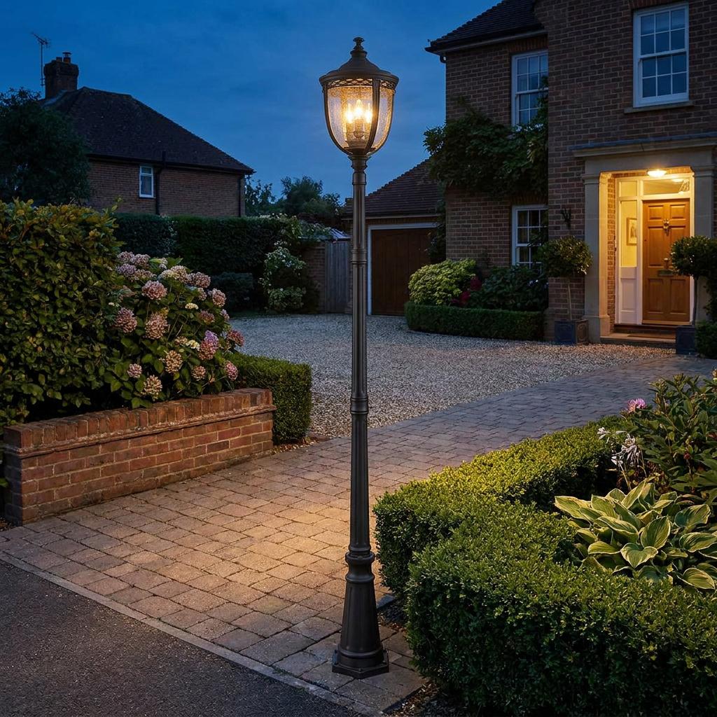 Feiss English Bridle black lamp post lantern illuminating a brick house driveway at night, surrounded by lush gardens.