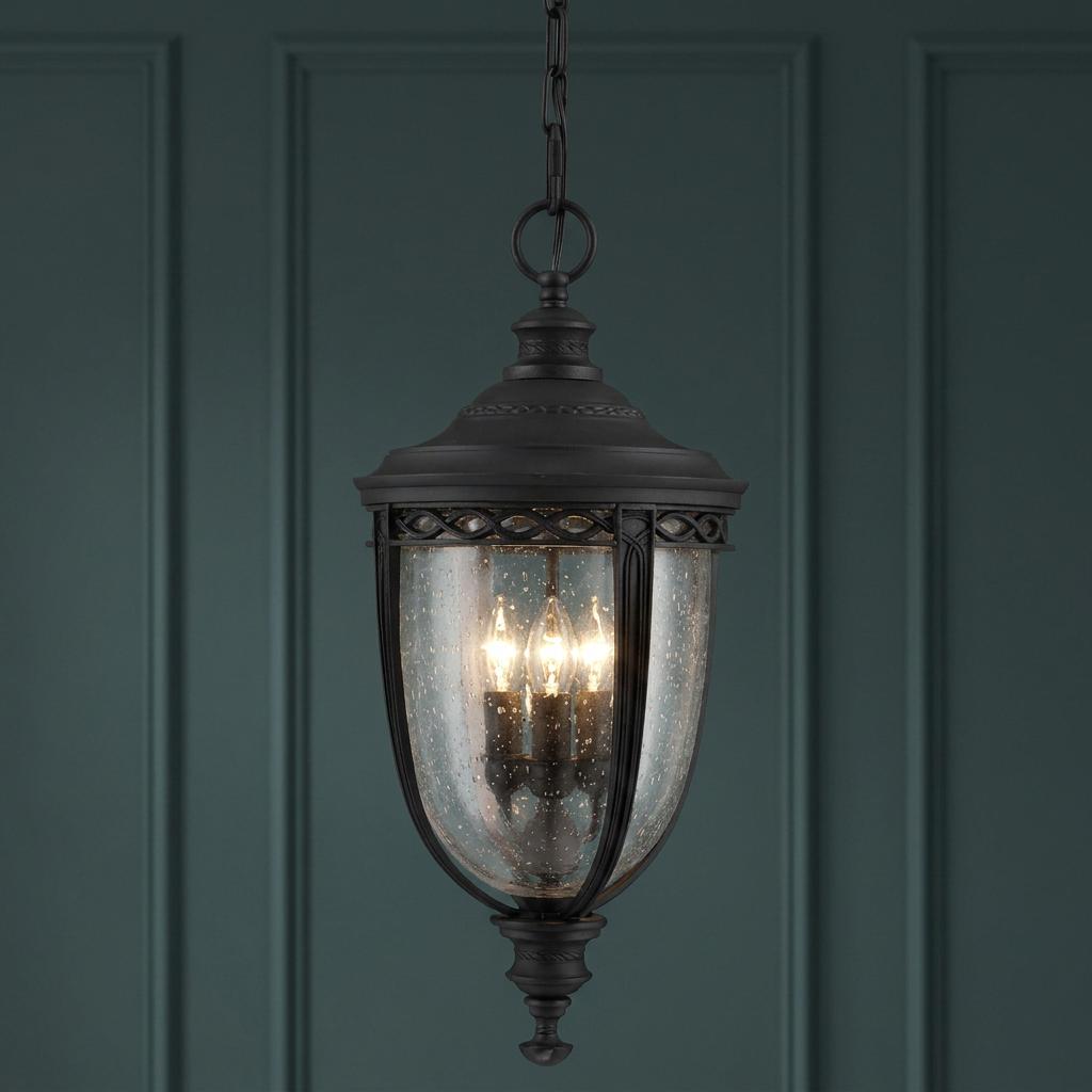 Feiss English Bridle black outdoor pendant lantern with seeded glass, hanging against a dark green paneled wall.