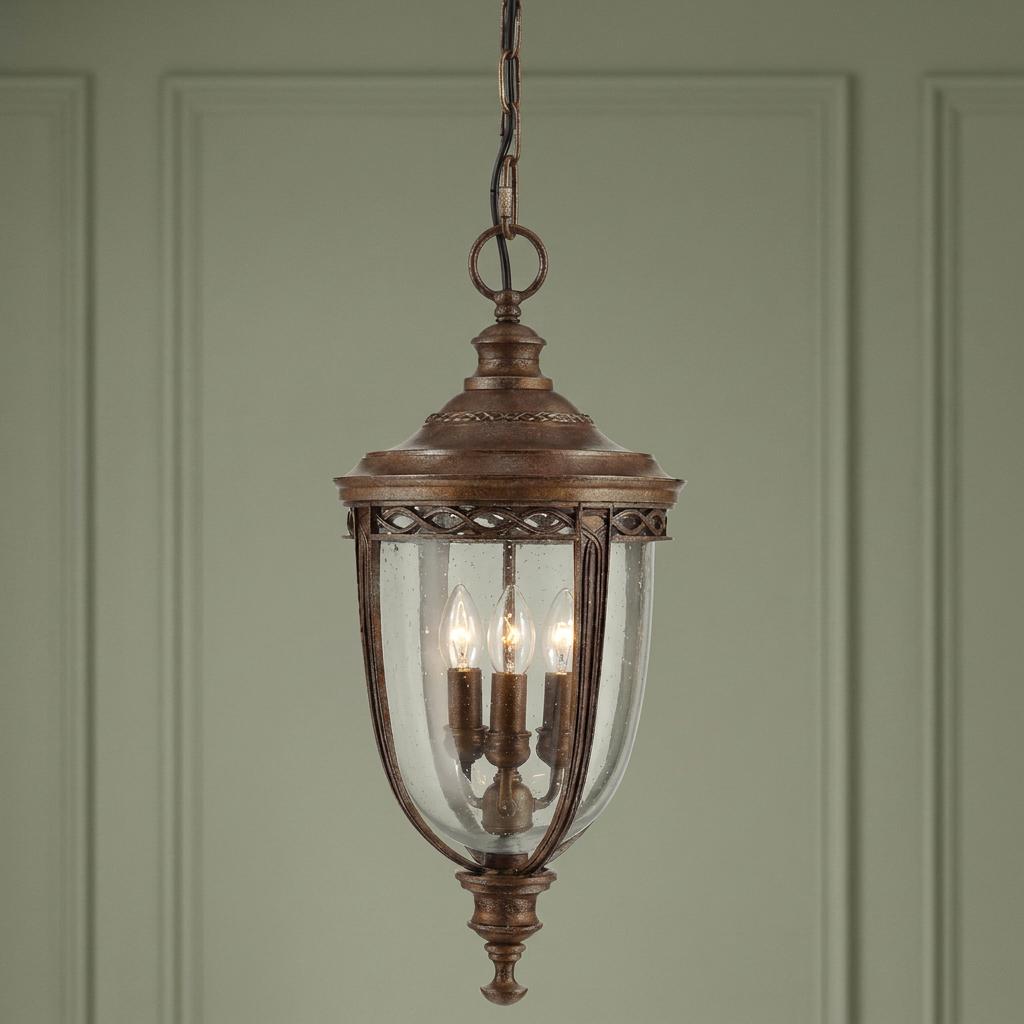 Feiss English Bridle bronze outdoor pendant light with seeded glass and lit bulbs against a green wall.