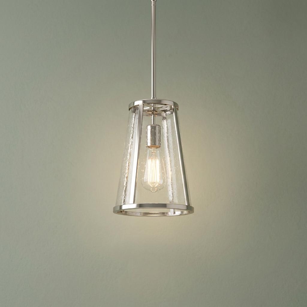 Polished nickel lantern pendant with seeded glass and a lit Edison bulb against a sage green wall.