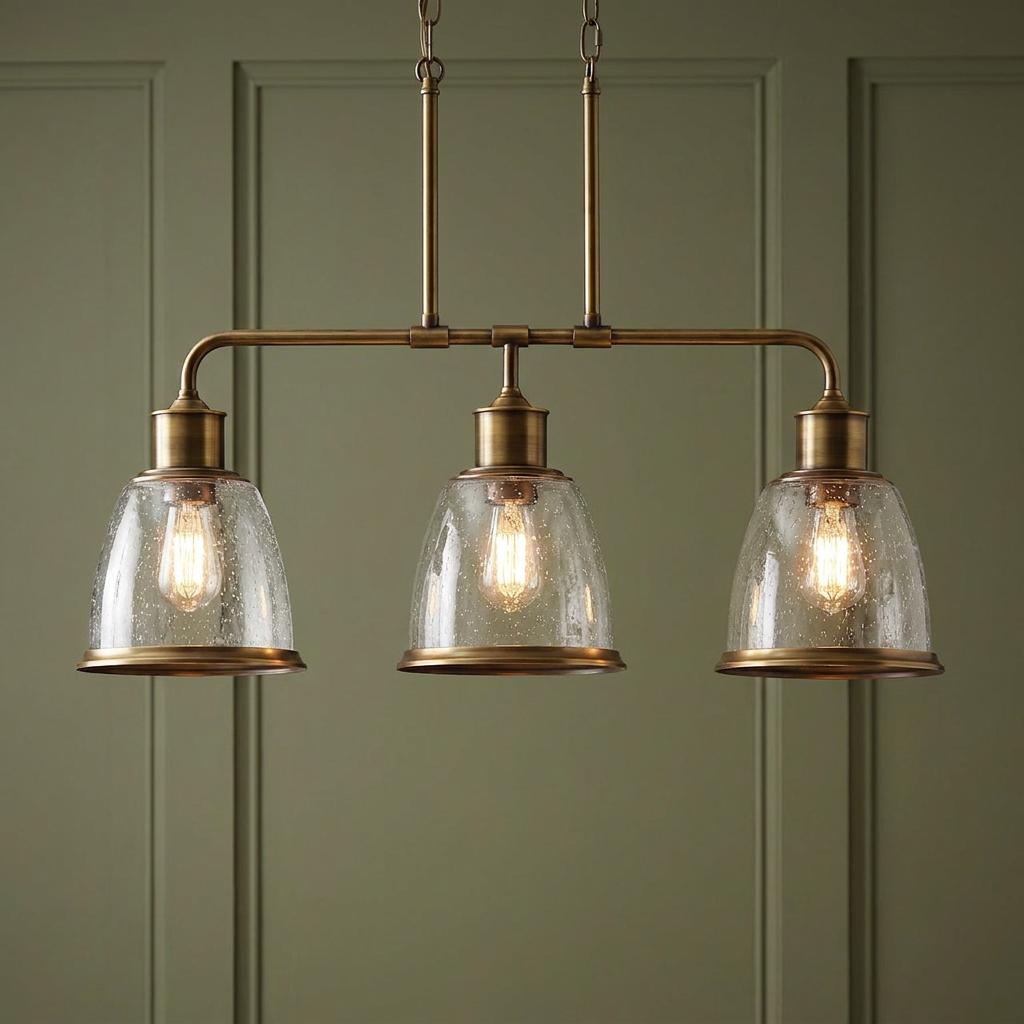 Three-light brass island pendant with seeded glass bell shades against a sage green paneled wall.