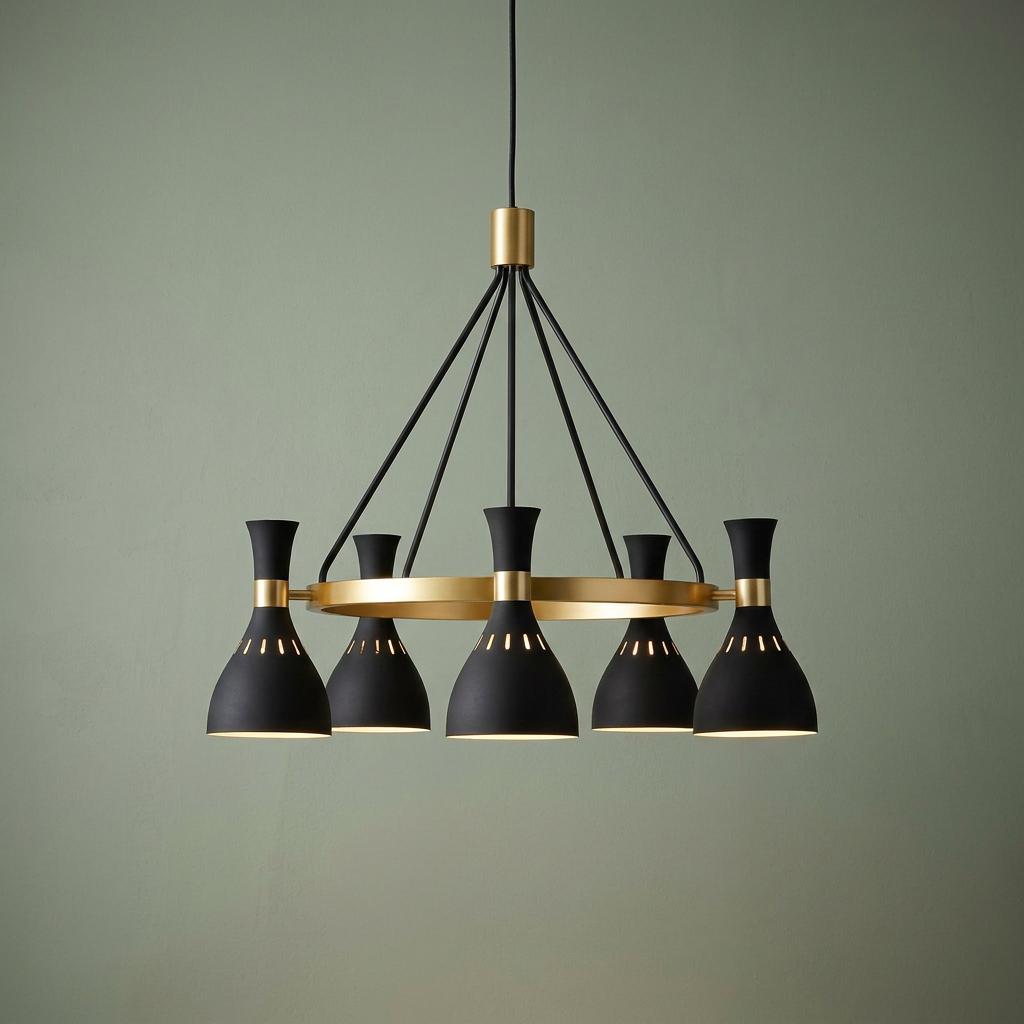Modern five-light chandelier with black hourglass shades and brass accents, hanging against a soft green wall.