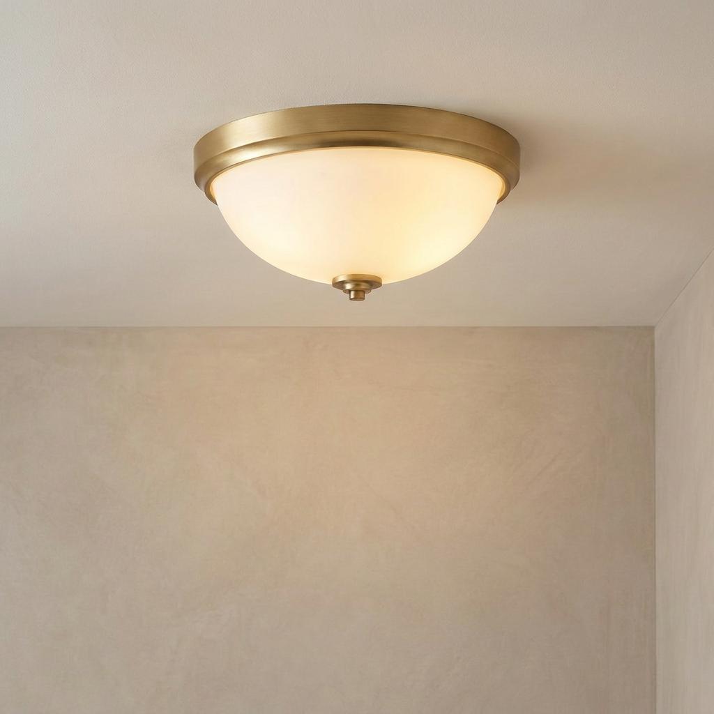 Brushed brass bathroom ceiling light with a white frosted glass dome shade mounted on a neutral ceiling.