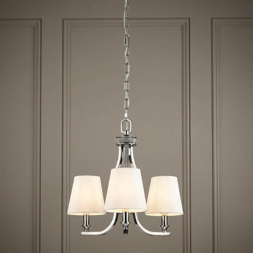 Three-light polished nickel chandelier with white tapered fabric shades suspended by a chain against a paneled wall.