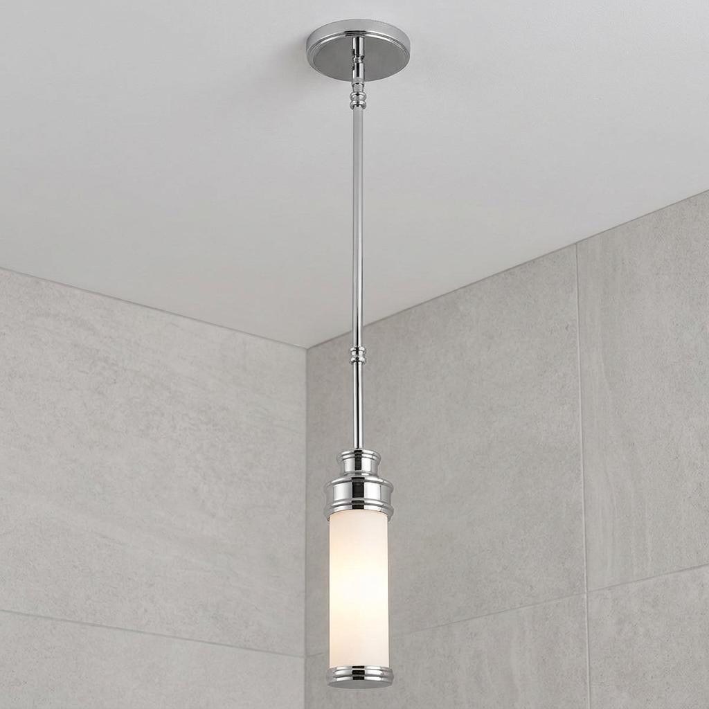 Chrome mini pendant light with a white cylindrical glass shade hanging against a grey tiled bathroom wall.
