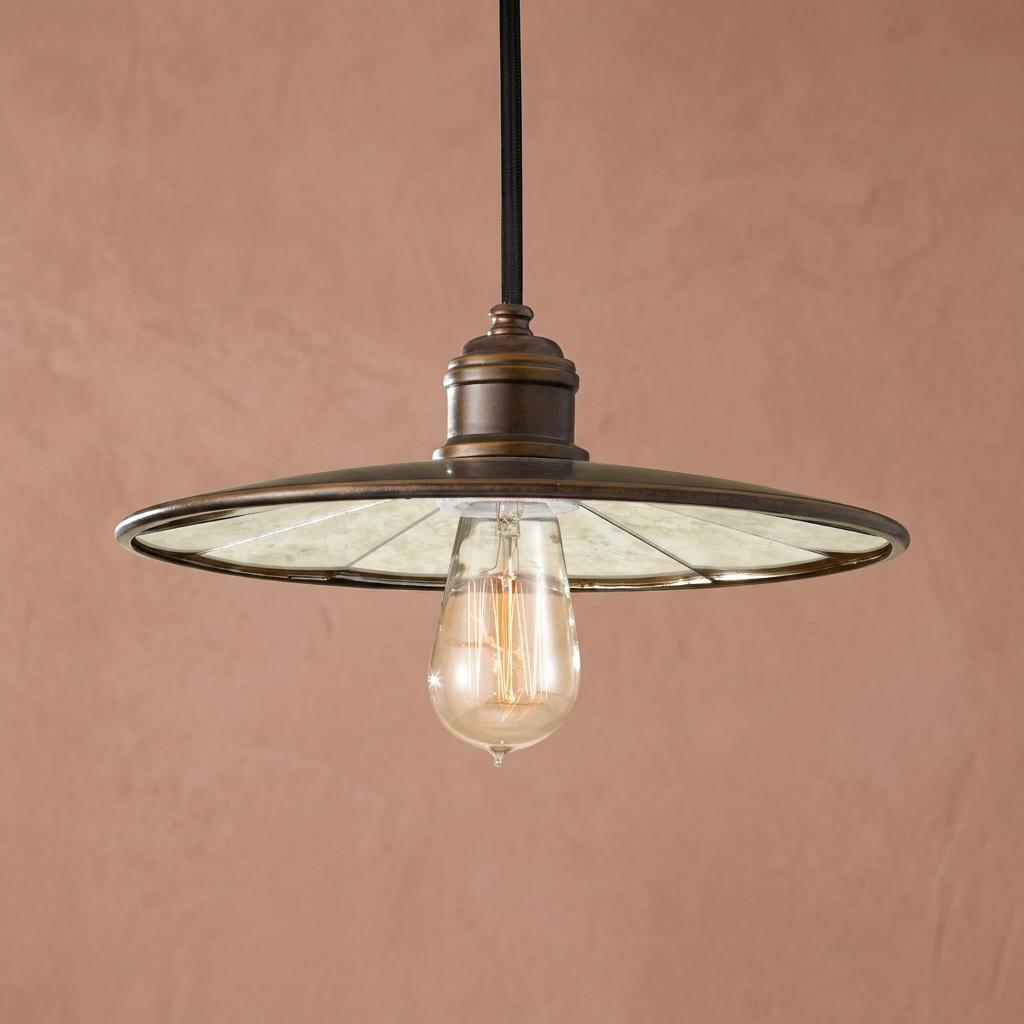 Industrial bronze pendant light with a mirrored saucer shade and Edison bulb, set against a pink textured wall.