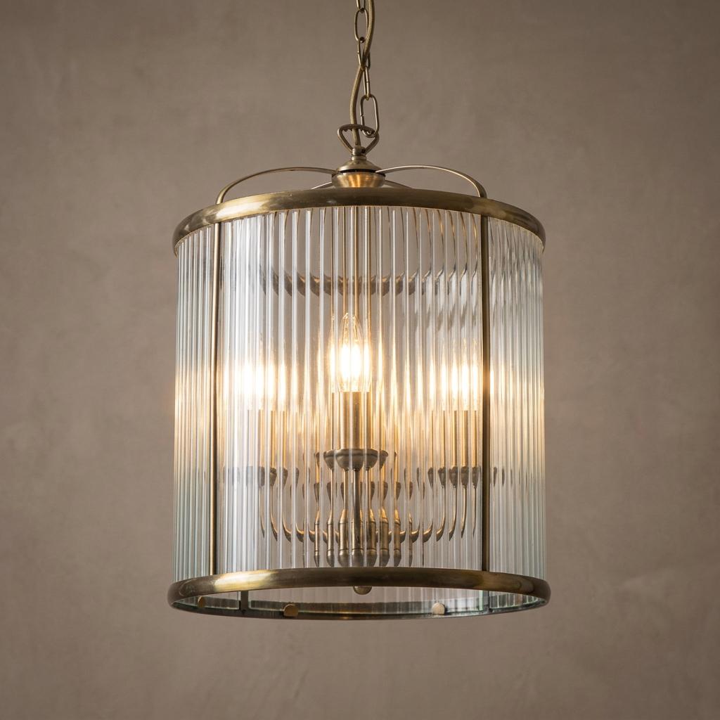 Antique brass 4-light hallway lantern with a ribbed cylindrical glass shade hanging against a neutral wall.