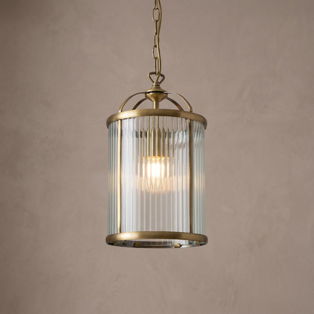 Antique brass pendant light with a ribbed glass cylinder hanging against a neutral wall.