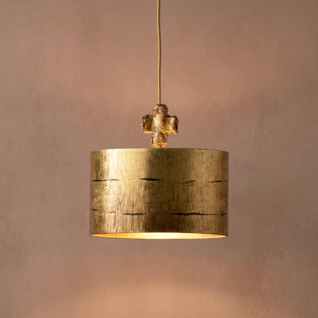 Gold cylindrical pendant light with a textured finish and cross finial glowing against a neutral background.