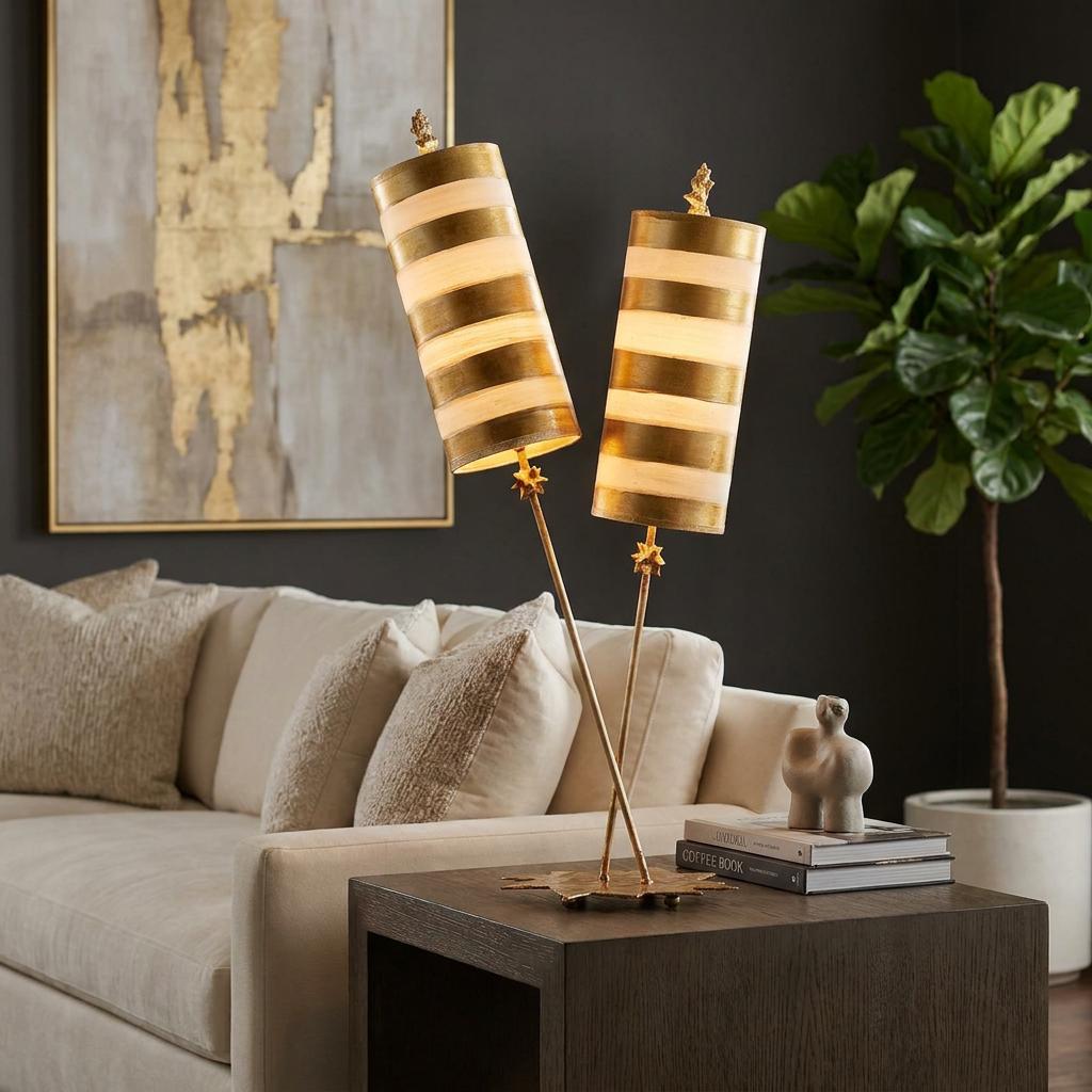 Gold table lamp with dual stems and striped cylinder shades on a wooden side table in a living room.