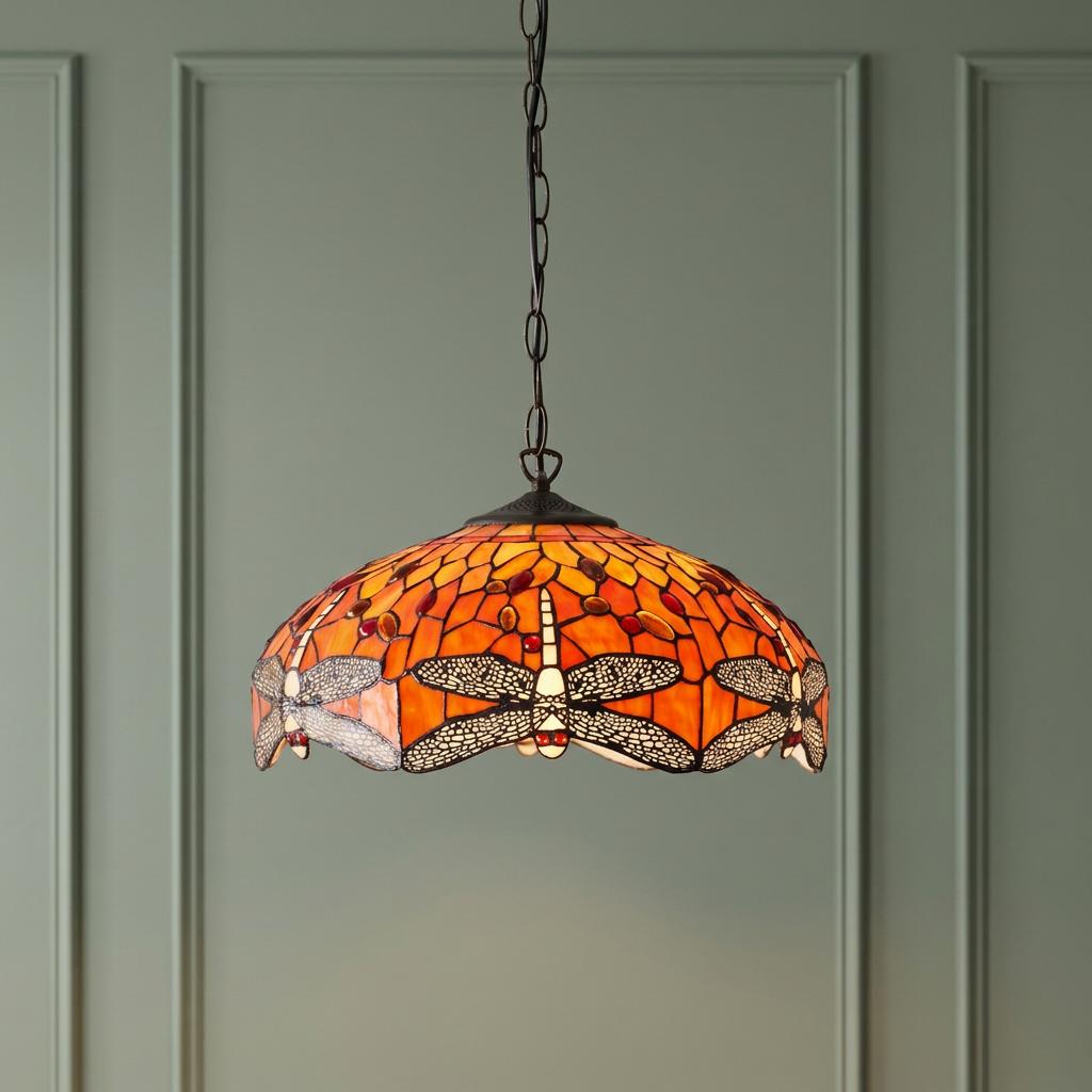 Flame Dragonfly Tiffany pendant light with an orange stained glass dragonfly shade hanging against a green wall.