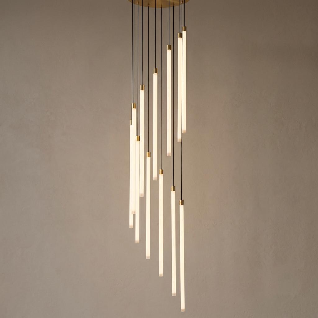 A modern multi-pendant chandelier with illuminated vertical white tubes cascading from a brass mount.