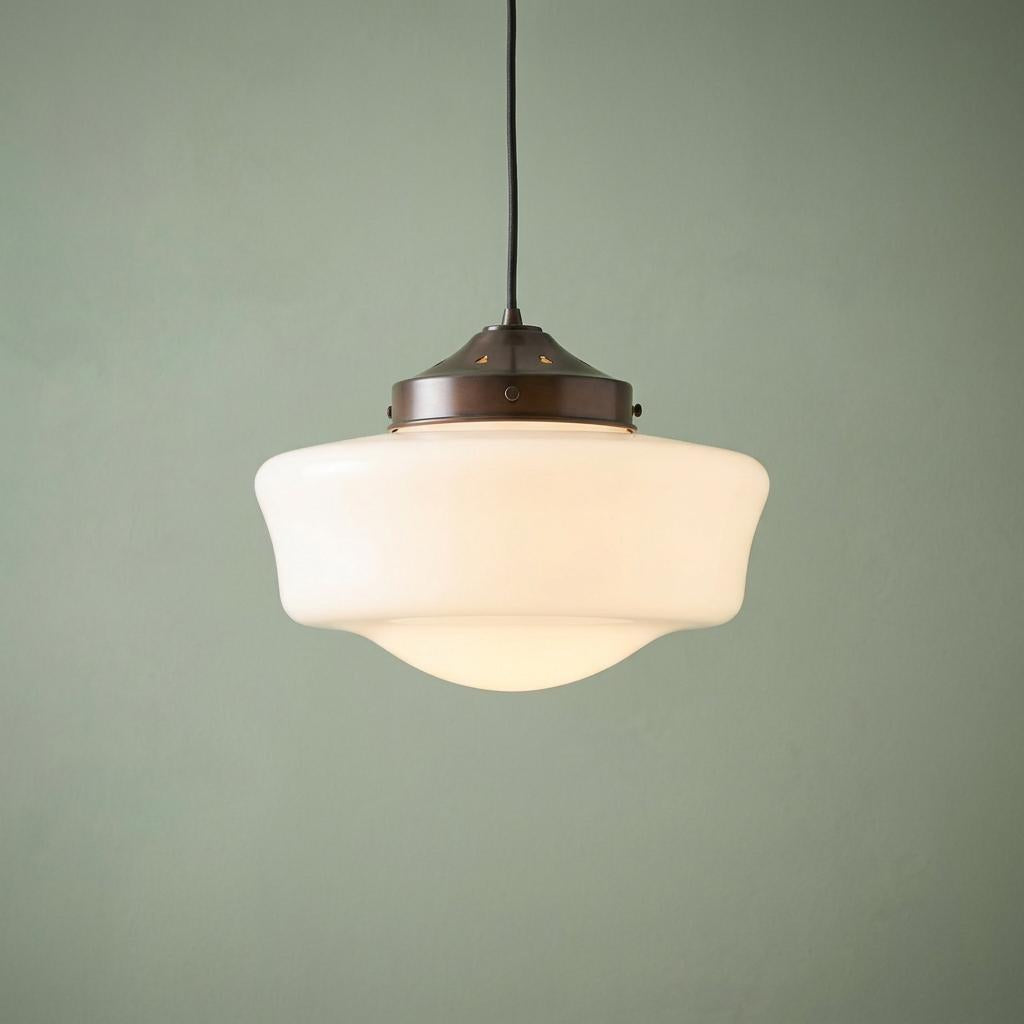 Flashed opal schoolhouse pendant light with dark bronze fixing hanging against a sage green wall.