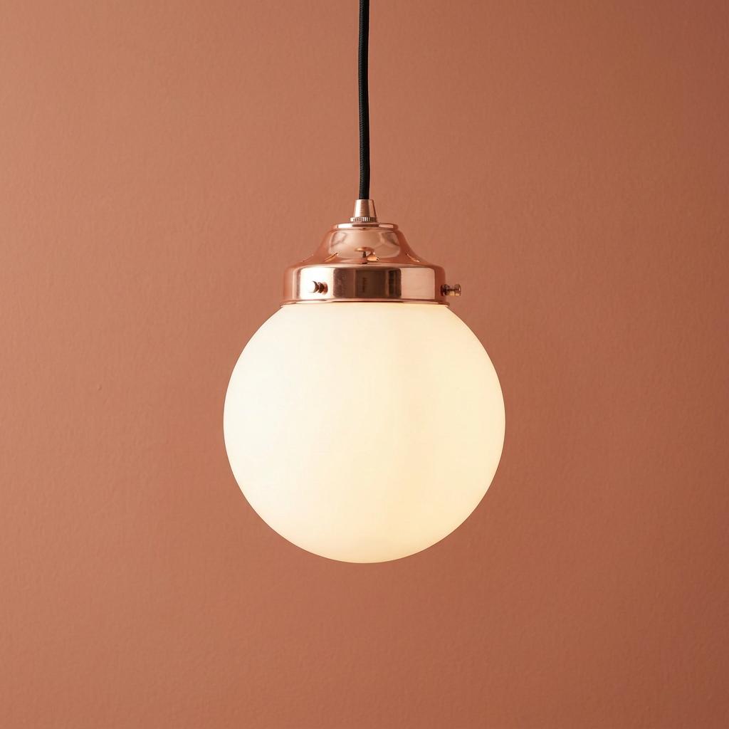 White opal glass globe pendant light with copper hardware against a terracotta background.