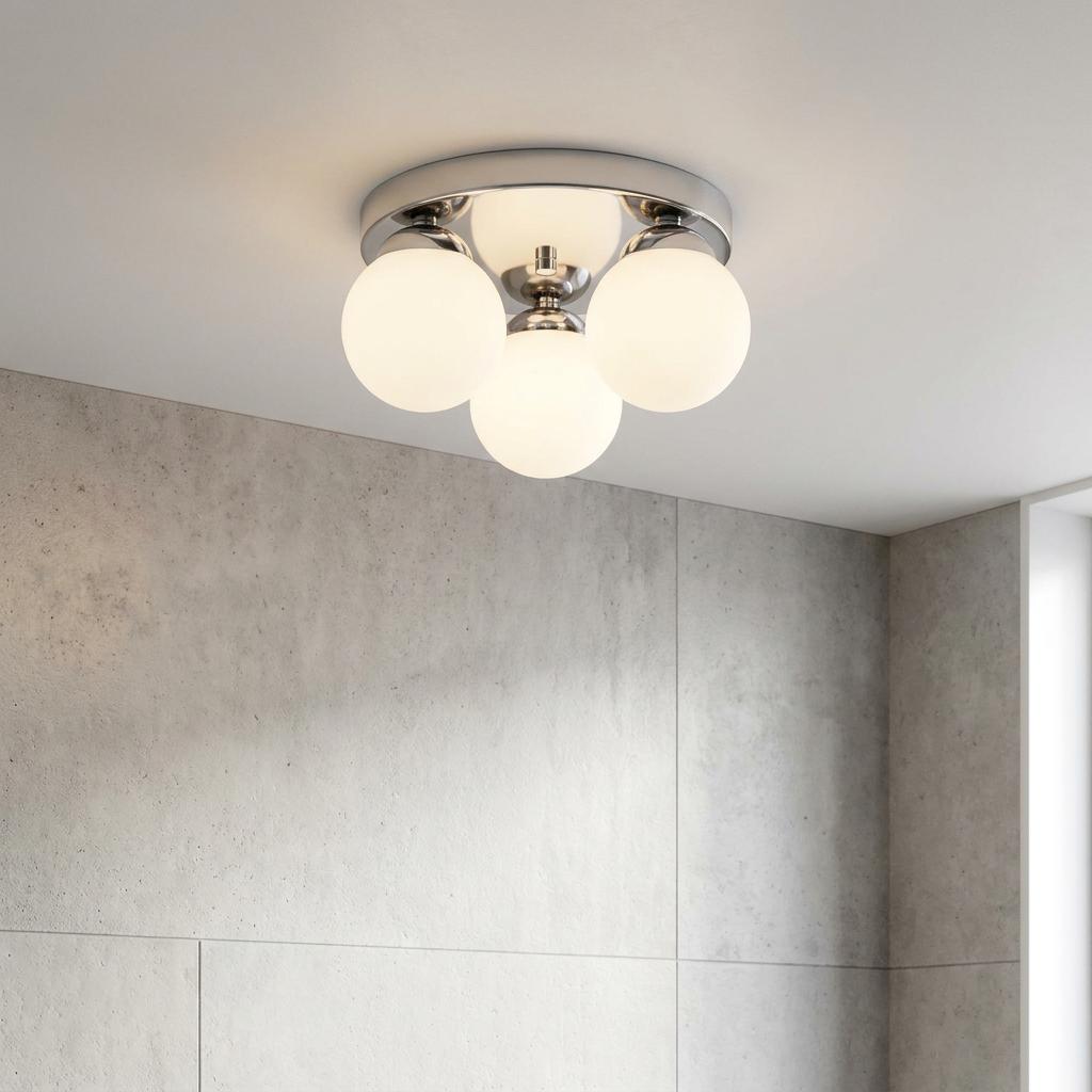 Modern chrome flush ceiling light with four frosted glass globes mounted in a bathroom with grey tiled walls.