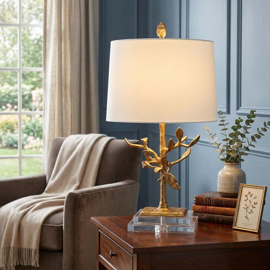 Gilded tree-branch table lamp with a white drum shade on a wooden side table in a cozy living room.