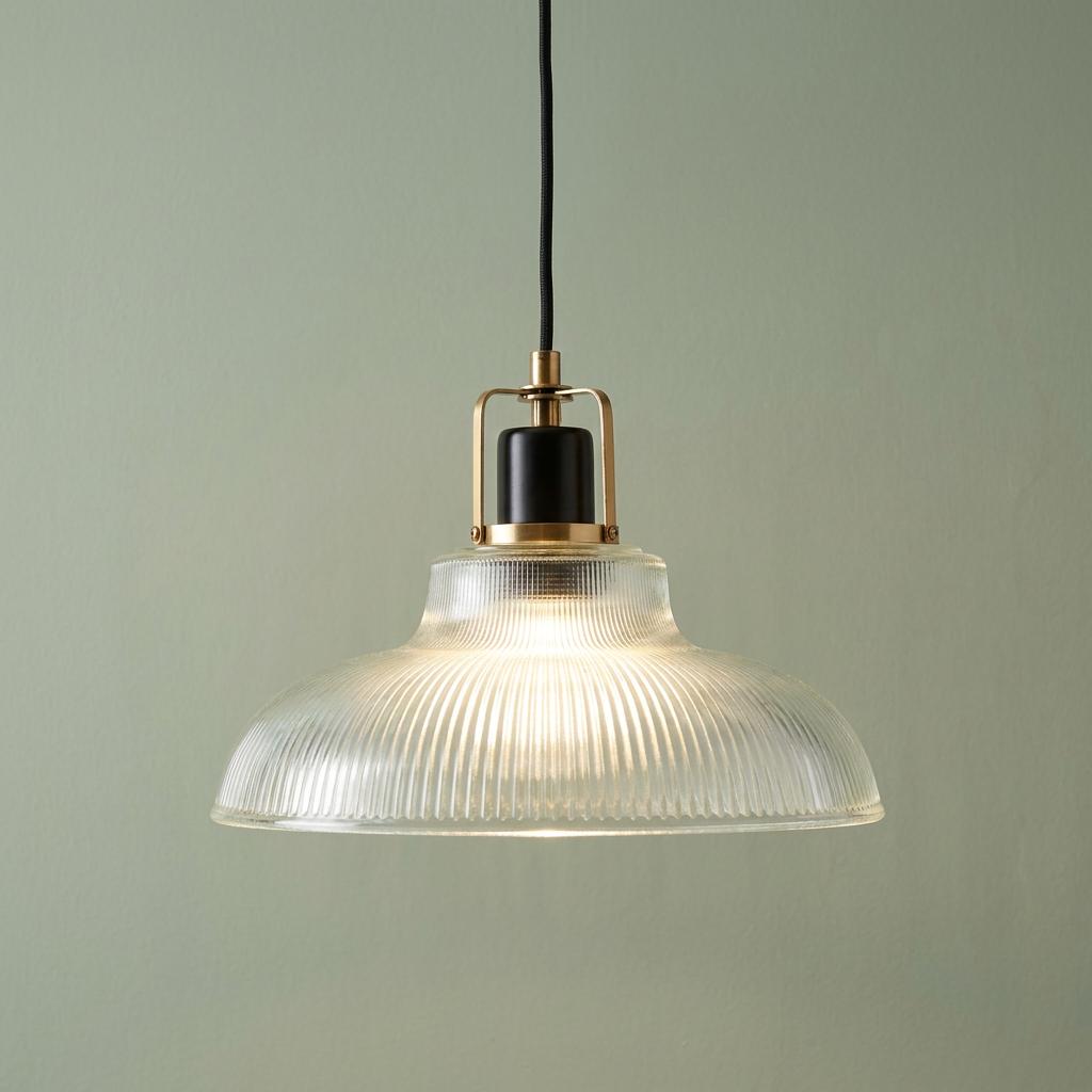 Ribbed clear glass pendant light with brass and black accents hanging against a pale green wall.
