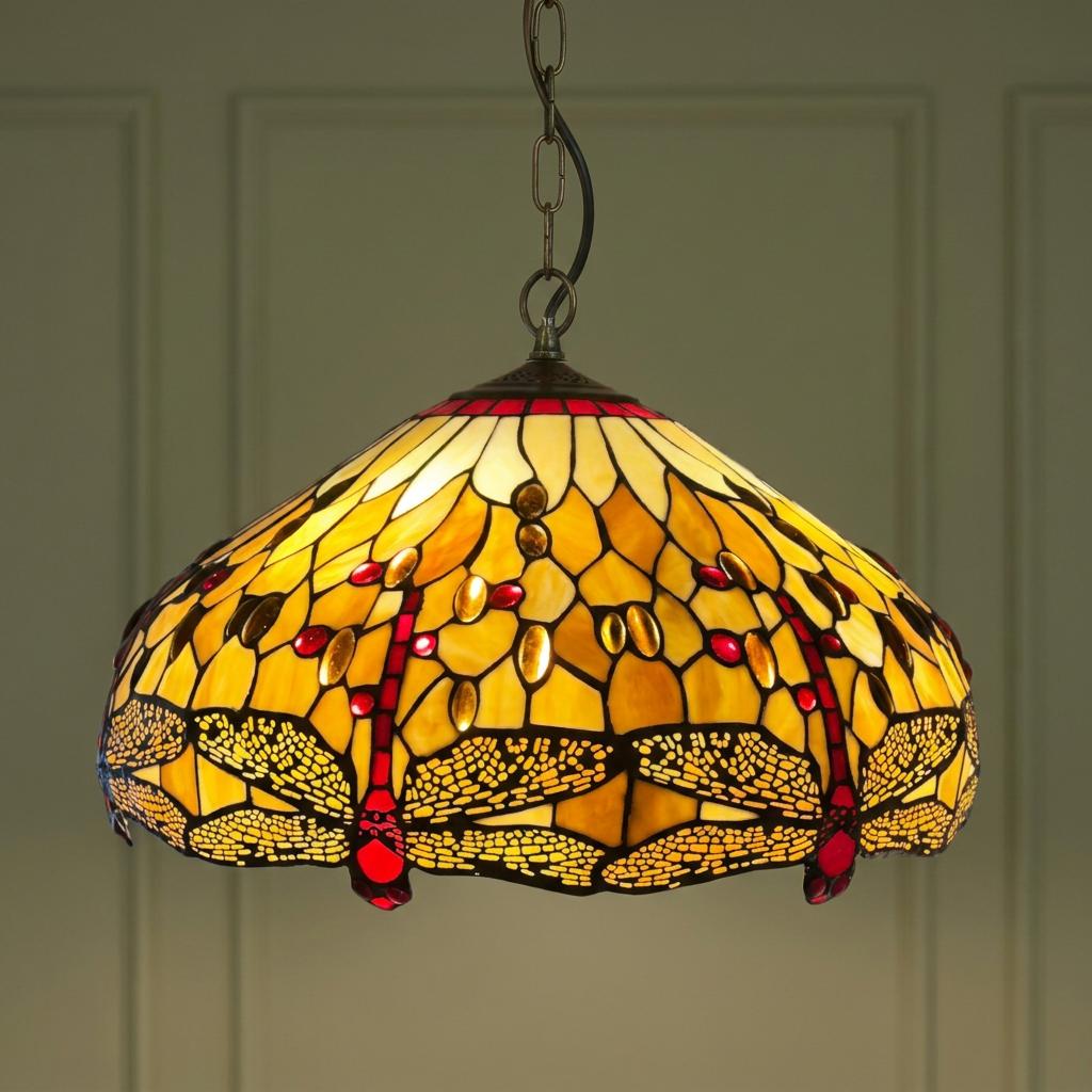 Illuminated Golden Dragonfly Tiffany pendant light with amber stained glass and red jewel accents.
