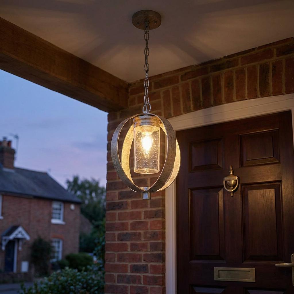A rustic orb pendant light with a seeded glass shade illuminates the entrance of a brick house at dusk.