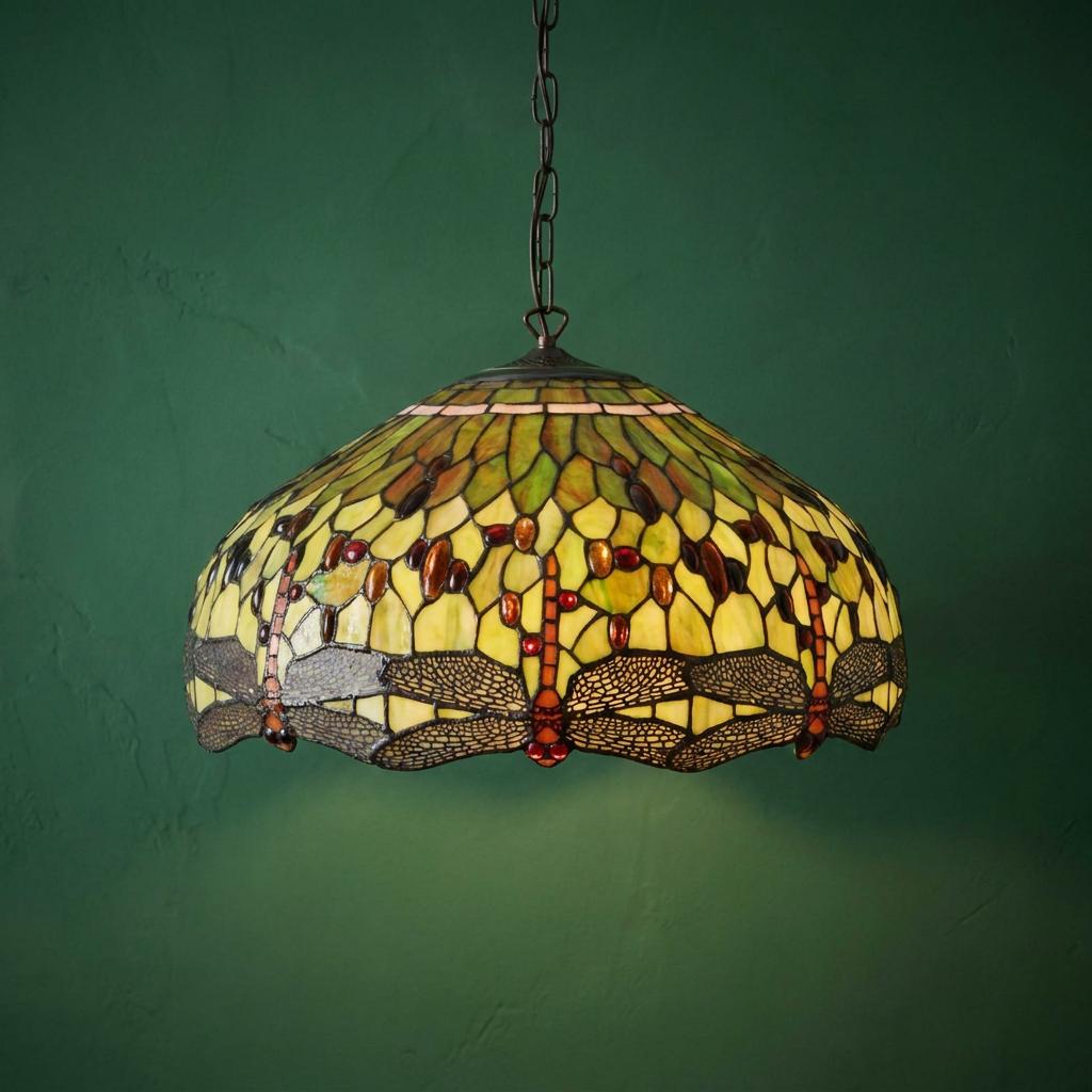 Intricate green dragonfly Tiffany ceiling light with amber jewels against a green textured wall.