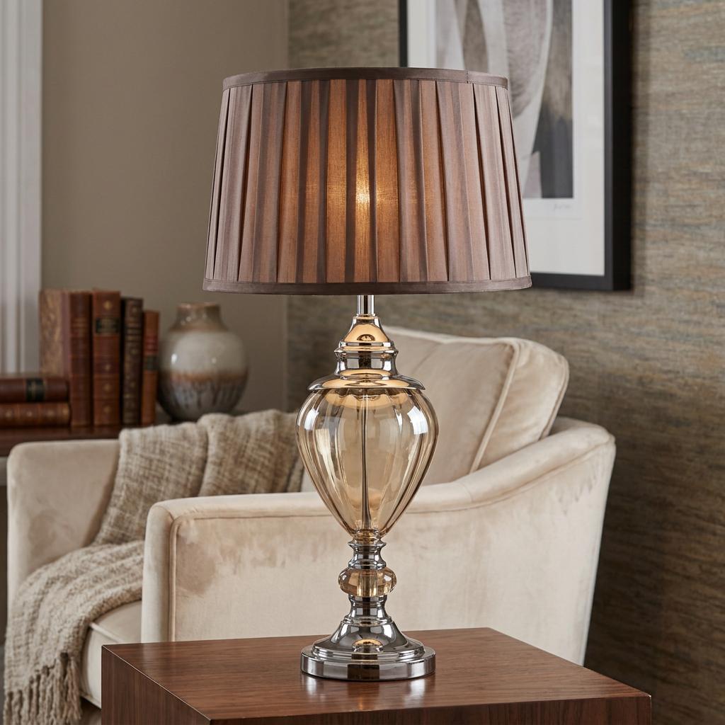 Amber glass urn table lamp with a brown pleated shade, illuminated on a wooden table in a cozy living room.