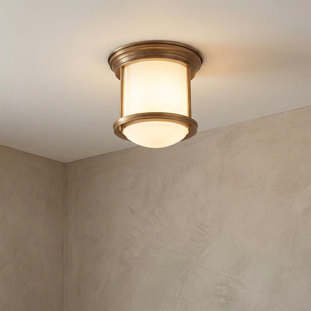 Hadrian flush bathroom ceiling light with brushed bronze frame and glowing opal glass on a white ceiling.