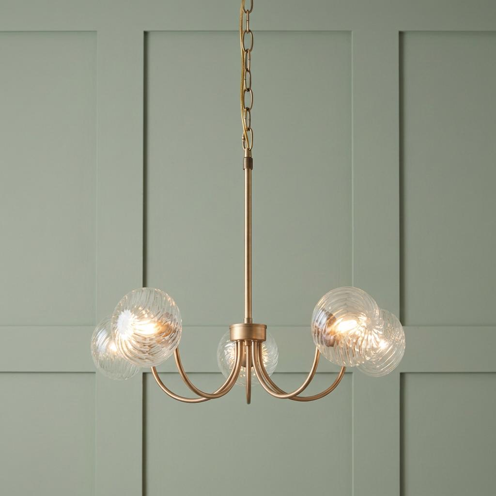Hague five-light brass pendant chandelier with ribbed glass globes against a sage green paneled wall.