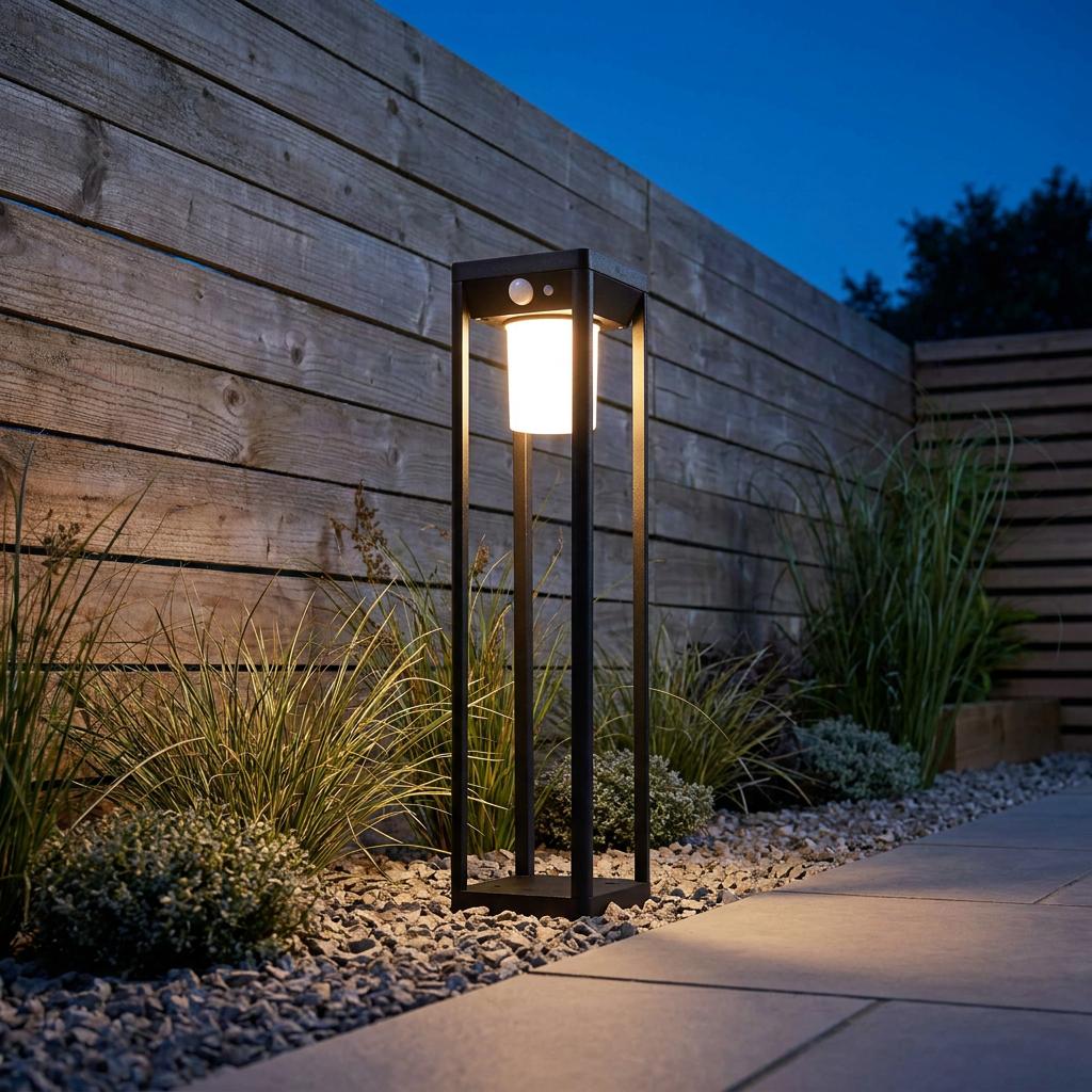 A black solar powered bollard light glows warmly at dusk in a gravel garden alongside a wooden fence.