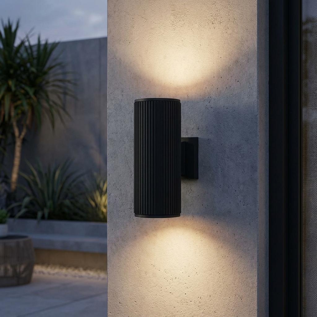 Black ribbed cylindrical up/down wall light mounted on a concrete pillar in a modern outdoor setting.