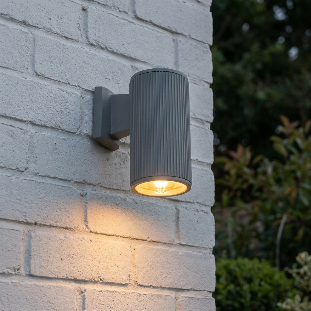 Grey ribbed cylindrical wall light mounted on a white brick wall, casting a warm downward glow.