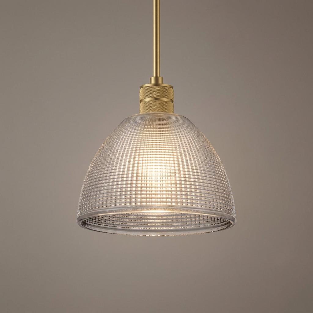 Brass pendant light with a domed prismatic smoke glass shade glowing against a neutral gray background.