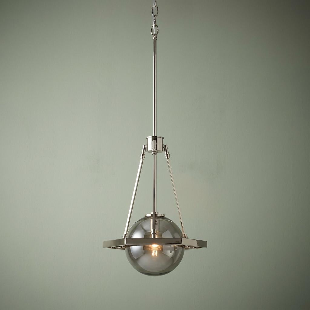 Polished nickel ceiling pendant light with a smoked glass globe and orbital ring frame against a green wall.