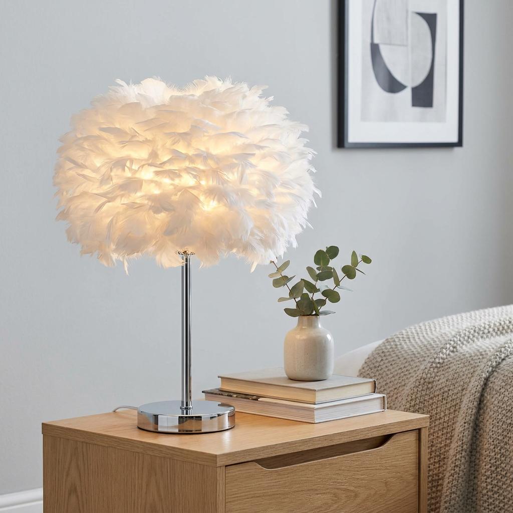 Hattie Table Lamp with a fluffy white feather shade and chrome base lit on a wooden nightstand.