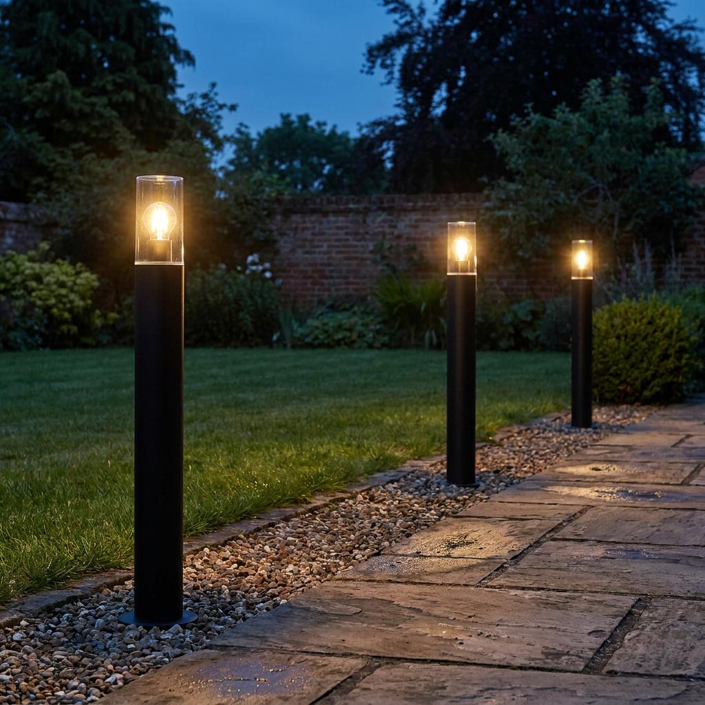 Three black Hayden bollard lights with warm glowing glass tops lining a stone garden path at dusk.