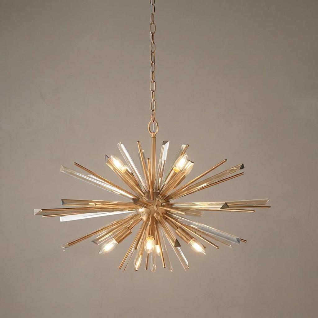 Starburst chandelier with antique brass spikes and clear glass prisms illuminated against a neutral wall.