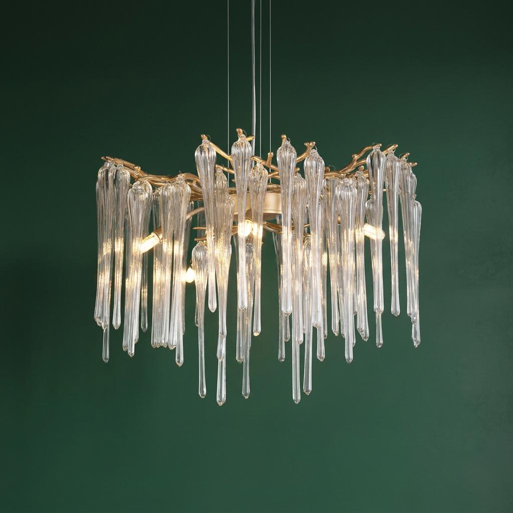 A gold chandelier with long, icicle-like clear glass drops suspended against a dark green wall.