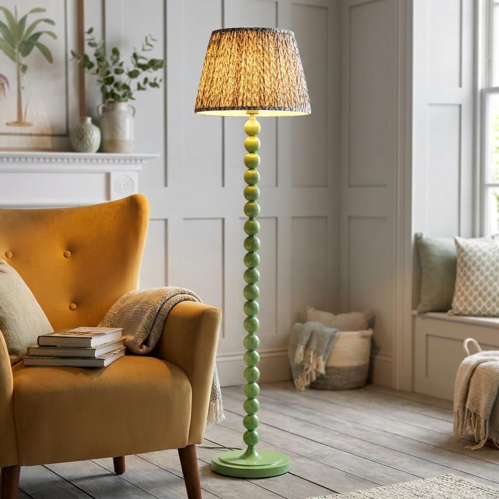Green bobbin floor lamp with a grey leaf shade standing next to a yellow armchair in a cozy living room setting.
