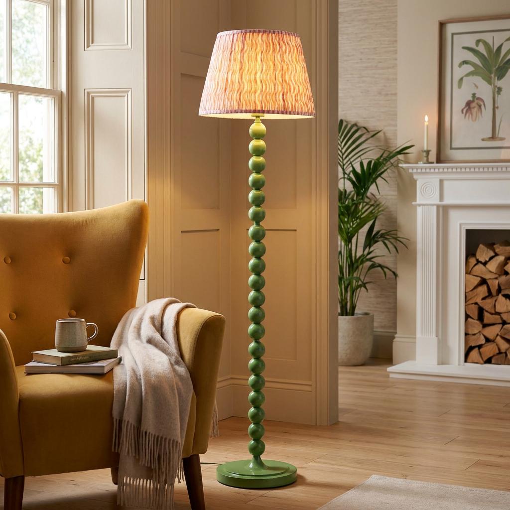 Green bobble floor lamp with a coral pink ripple shade standing in a living room next to a yellow armchair.