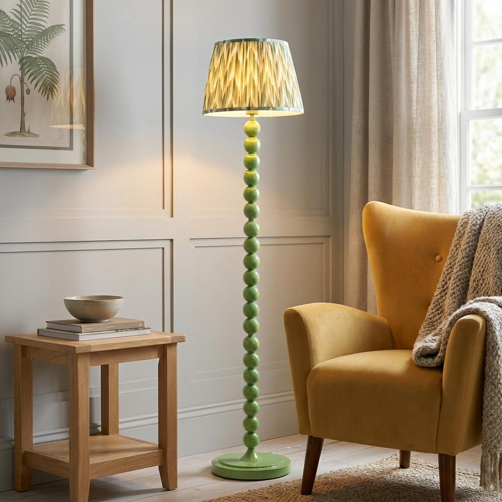Green bobbin floor lamp with a zigzag shade next to a yellow armchair in a paneled living room.