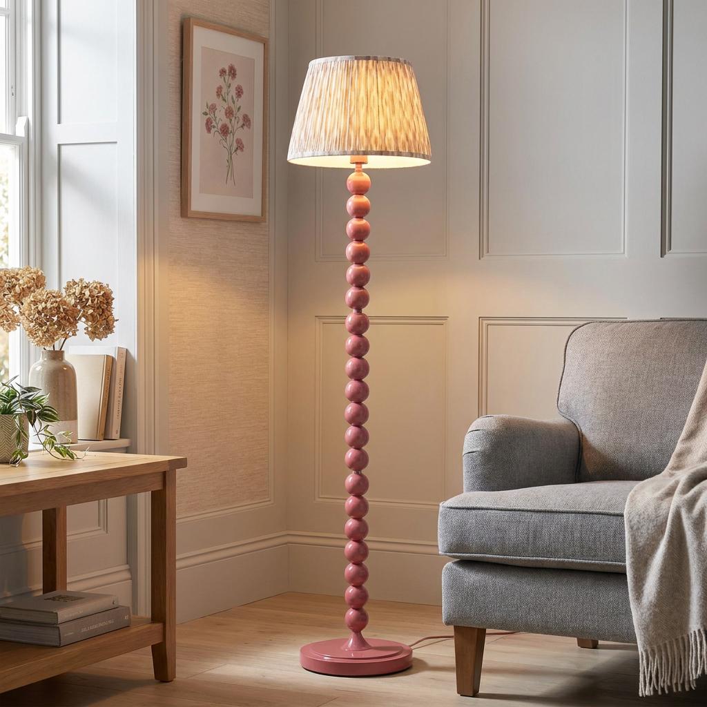 Pink floor lamp with a beaded stem and ikat shade standing beside a grey armchair in a panelled living room.