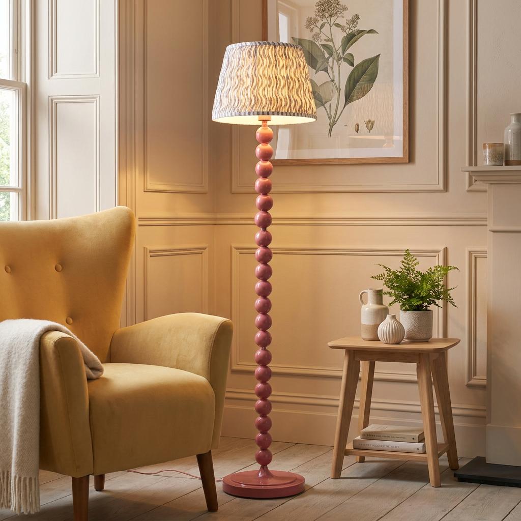 Higgledy pink bobbin floor lamp with a grey ripple shade by a yellow armchair in a neutral-toned living room.