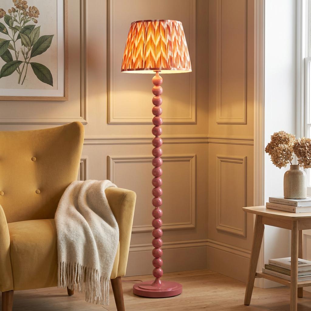 Pink bobbin-style floor lamp with an orange zigzag shade next to a yellow armchair in a cozy living room.