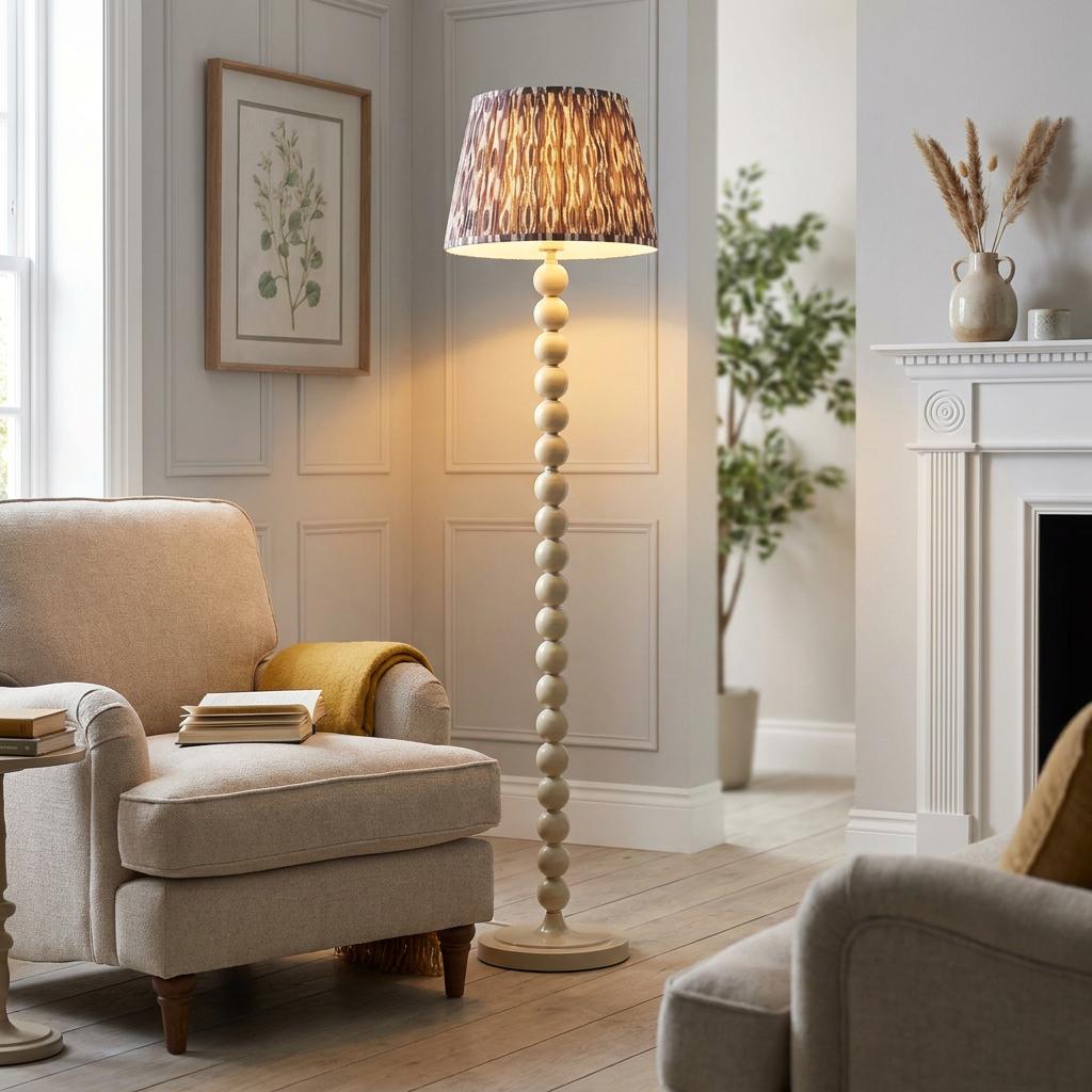 White bobbin floor lamp with a grey ikat shade beside a beige armchair in a modern living room.