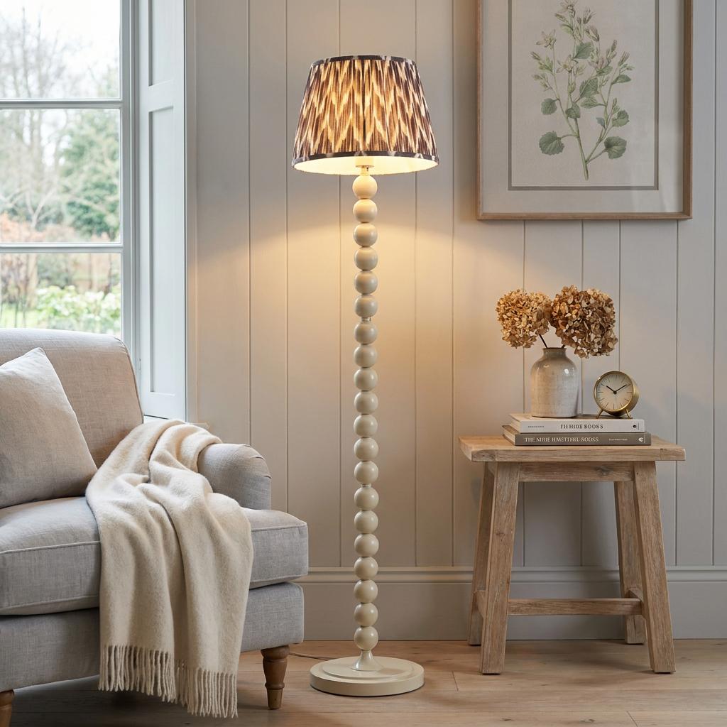 White bobbin-style floor lamp with a zigzag shade illuminating a cozy living room next to a grey armchair.