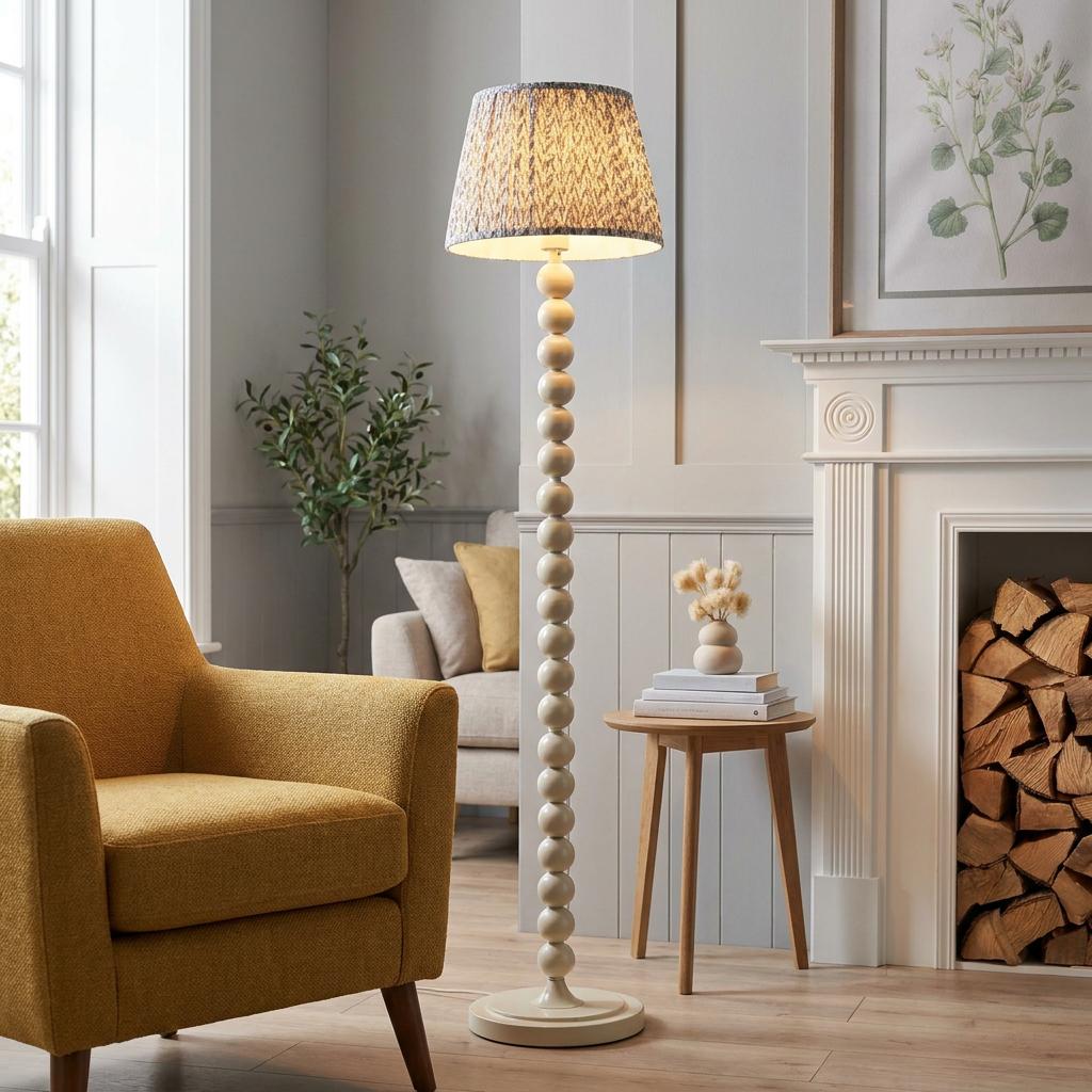 White bobbin floor lamp with a grey leaf-patterned shade in a living room next to a yellow armchair.
