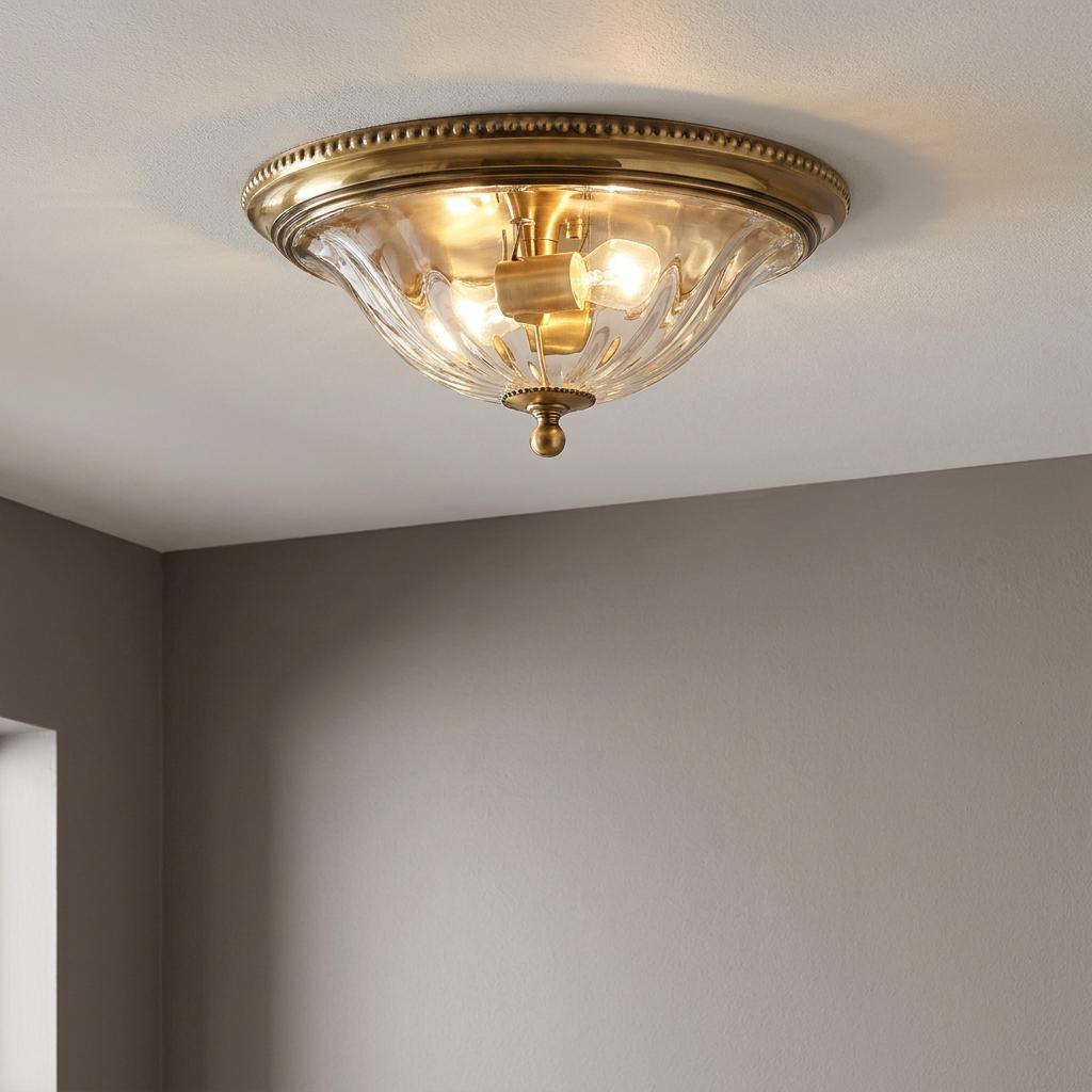 Hinkley Cambridge brass flush ceiling light with clear ribbed glass shade and beaded trim, illuminated.